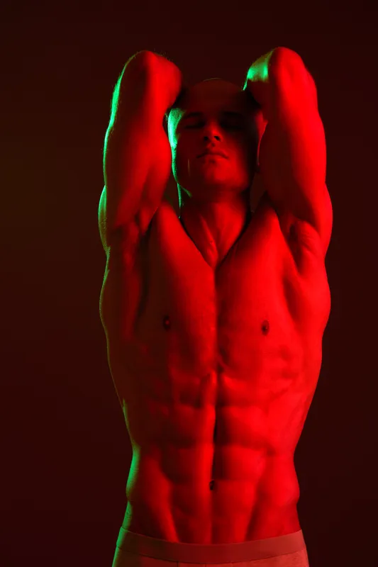 Muscular man posing under vibrant lights, showcasing strength and confidence in a striking red hue. Perfect for fitness or wellness themes.