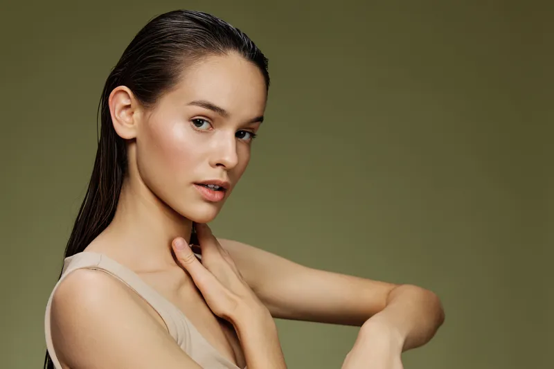 A young woman with long, wet hair, expressing calm and confidence against a soft green background, showcasing natural beauty and simplicity in fashion