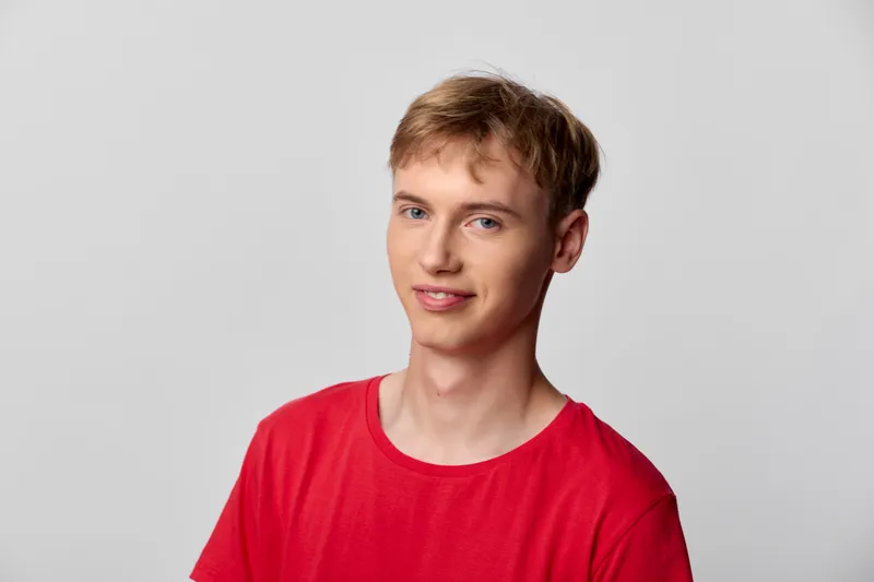 Smiling young man in a red shirt stands in a bright studio with a clean background, casual pose, and friendly expression, suitable for lifestyle, fashion, or tech campaigns
