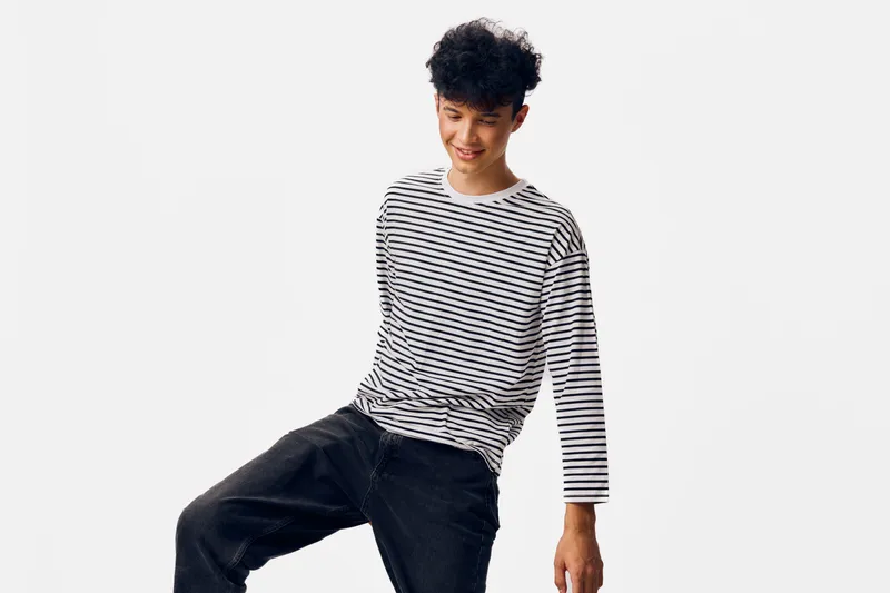 young man in striped shirt standing against white background with cheerful expression and casual black pants, studio portrait, bright lighting