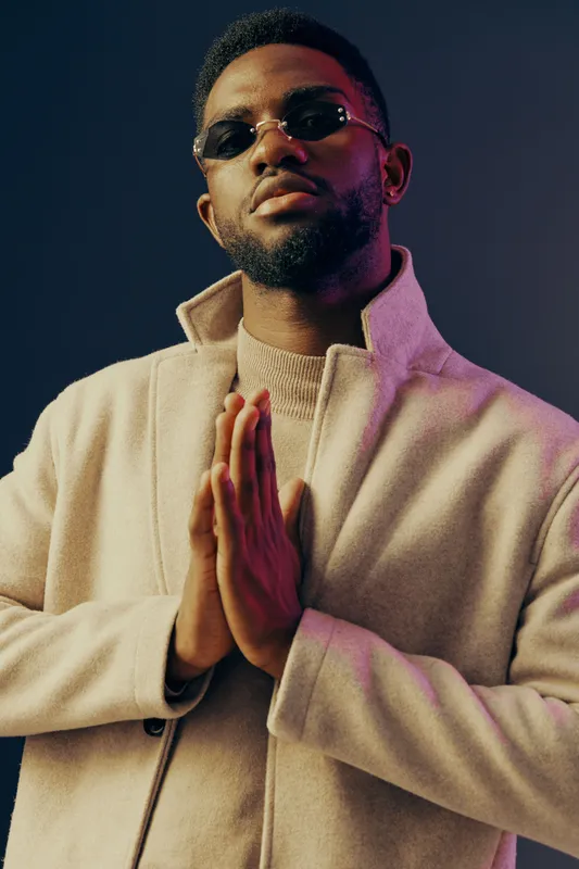 Stylish young man in a trendy coat with sunglasses, exuding confidence and elegance against a gradient background for fashion promotion