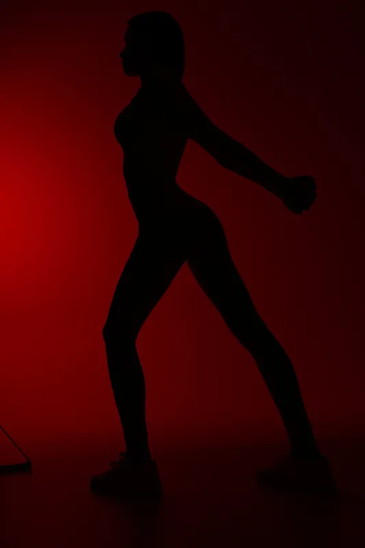 Silhouette of a woman sport fitness stretching against a red background, showcasing strength, flexibility, and athletic posture in a dynamic pose.