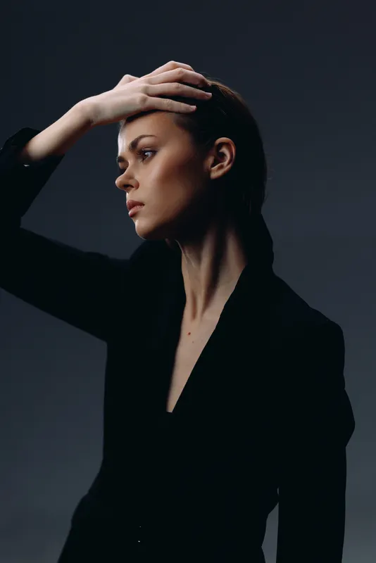 thoughtful woman in black posing with hand on head in dramatic lighting