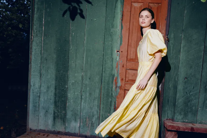Woman dress portrait at wooden doorway with flowing motion and fashion style in yellow gown natural soft light and authenticity inclusivity for editorial outdoor scene