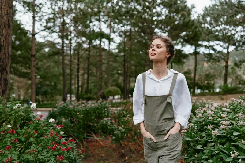 Young woman in casual outfit enjoying nature in a vibrant garden surrounded by flowers, showcasing a serene and joyful expression