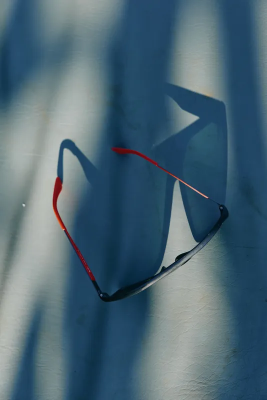 Casual sunglasses resting on a sunlit wall, sharp shadows create abstract shapes, relaxed mood, warm tones, minimalist scene, everyday accessory captured in natural light and color, photography mood