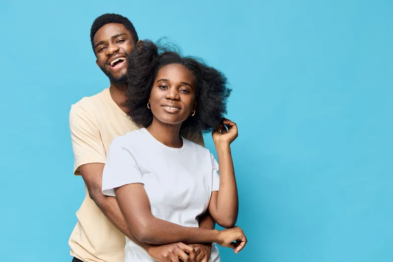 Happy couple posing together against a blue background, showcasing love and joy with vibrant clothing and natural hair