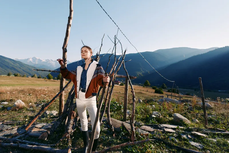 Woman nature mountains rural fence landscape traveler outdoors in a serene meadow, standing by rustic wooden posts wearing shearling jacket and boots for a peaceful travel portrait.