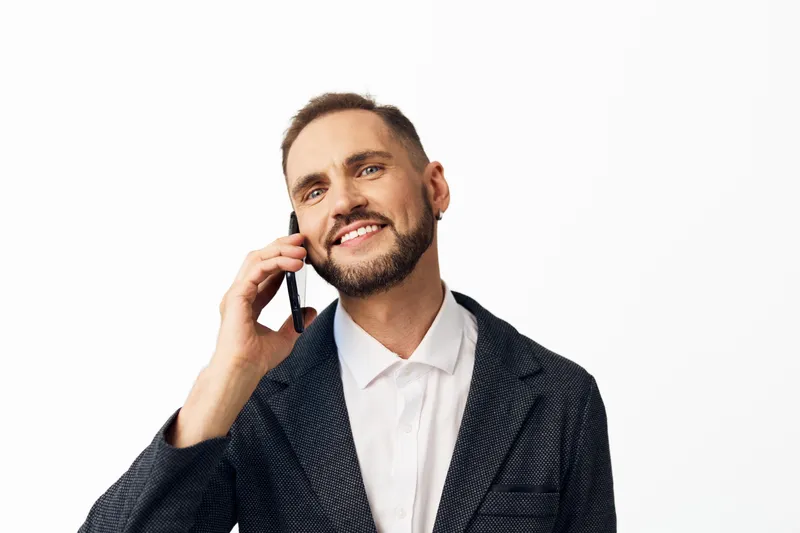 A confident business professional man on an isolated colored background, speaking on a mobile phone with a friendly smile, conveying focus, positivity, and everyday work confidence.