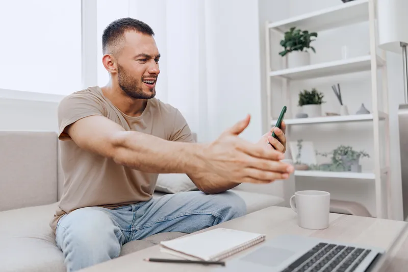 Engaged man communicating passionately, expressing emotions during a video call. Modern workspace with laptop and notebook, showcasing remote work dynamics with a personal touch.