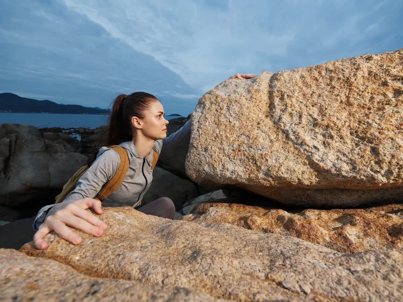 Young woman climbing rocks in athletic wear, showcasing determination and strength against a coastal backdrop Outdoors adventure in a natural setting