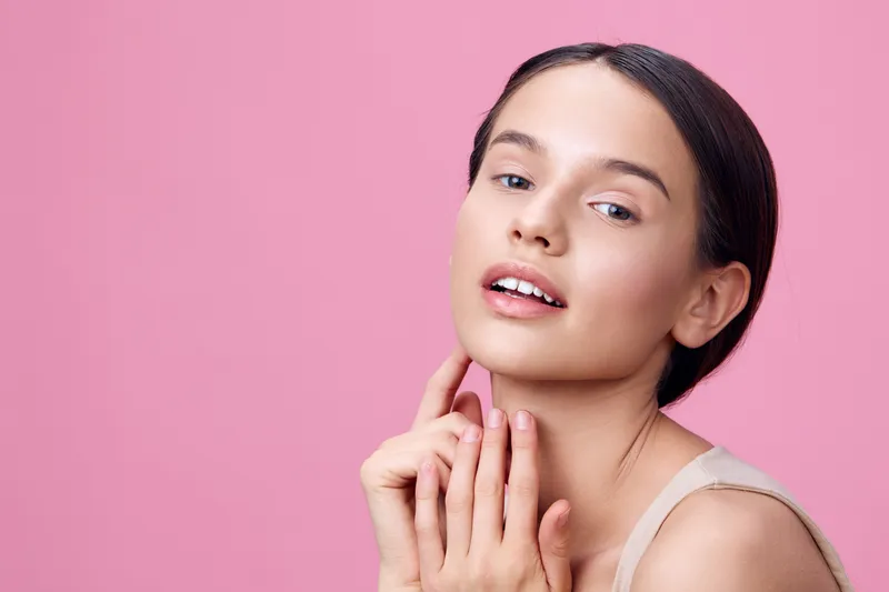 Young female model with natural makeup, expressing confidence against a soft pink background, showcasing beauty and self care concepts