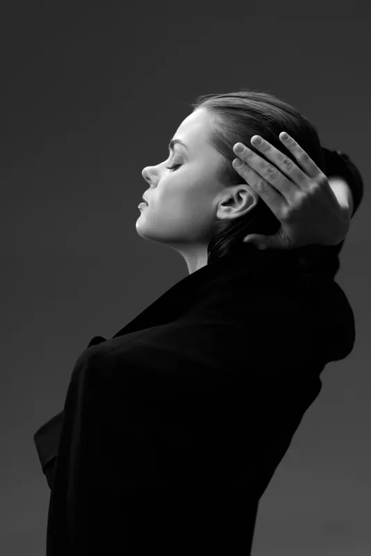 Black and white portrait of a calm woman with braided hair touching her head in a relaxed pose.