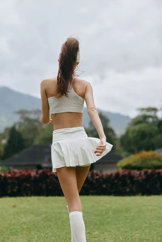 Elegant young woman in a sporty outfit, enjoying outdoor exercise in a lush green park, showcasing a healthy lifestyle with a bright smile