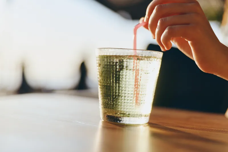 lifestyle woman enjoying refreshing drink in modern boho-western denim style with film color effect, street style vibe, natural light, casual summer moment