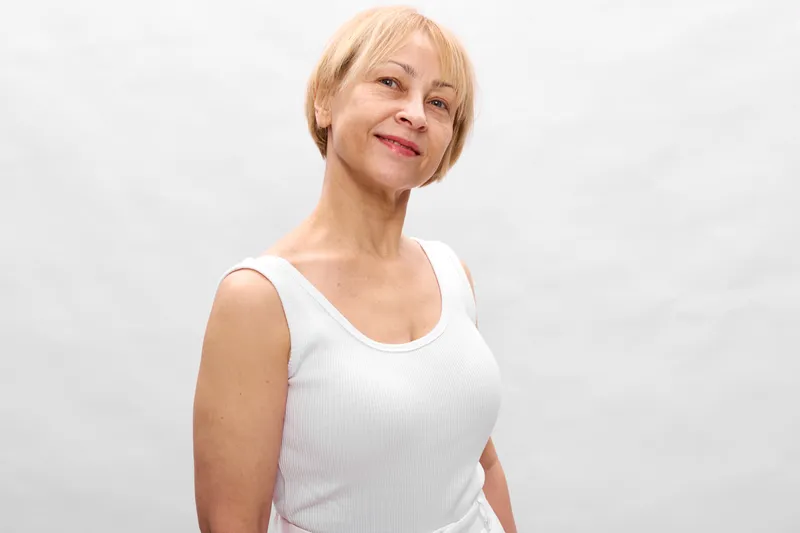 Elderly woman smiling portrait, short hair, white tank top, calm expression, studio light, soft neutral background, relaxed posture, front view, simple composition