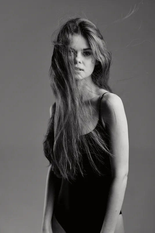 Black and white portrait of a young woman with long hair wearing a black outfit, expressing calm and introspective mood.