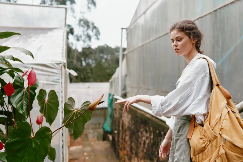 Young woman in a garden, exploring the beauty of flowers with a thoughtful expression while wearing a casual outfit and backpack, evoking a sense of serenity and connection to nature