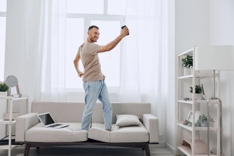 Energetic man enjoying music while dancing in a bright, modern living room. The atmosphere is joyful, showcasing a vibrant lifestyle. Perfect for upbeat content.