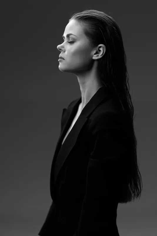 Black and white portrait of a serious woman with wet hair wearing dark clothing against a dark background