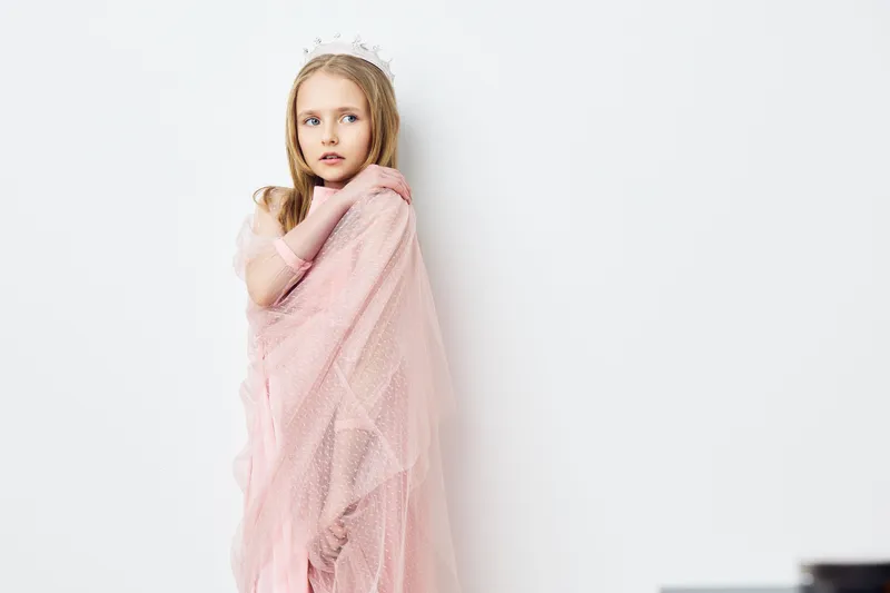 Young girl in a soft pink dress with a crown against a white background, expressing innocence and joy, perfect for children s photography and concepts of childhood