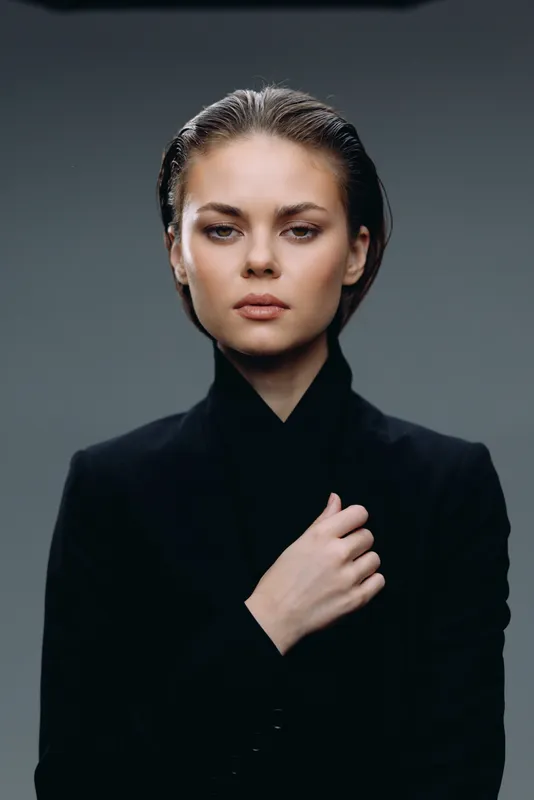 Serious woman in black jacket with confident look in studio portrait with neutral background