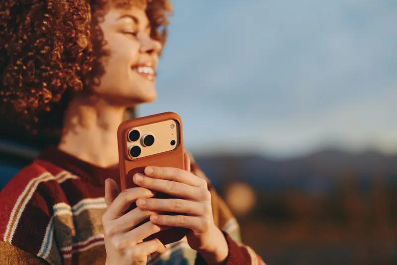 Woman lifestyle outdoors, curly hair smiling as she holds a phone for a selfie, striped sweater, warm autumn light, scenic landscape, soft breeze