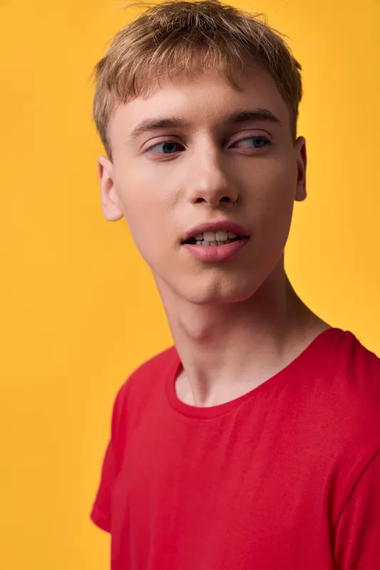 Young man wearing a red shirt against a warm yellow background, showcasing casual style, thoughtful expression and clean studio lighting. Modern lifestyle vibe with strong color contrast and minimal
