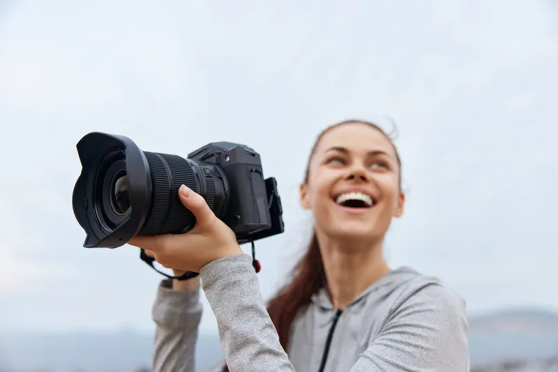 Happy young photographer enjoying outdoor photography, holding camera with joy in a bright gray outfit, capturing beautiful moments in nature