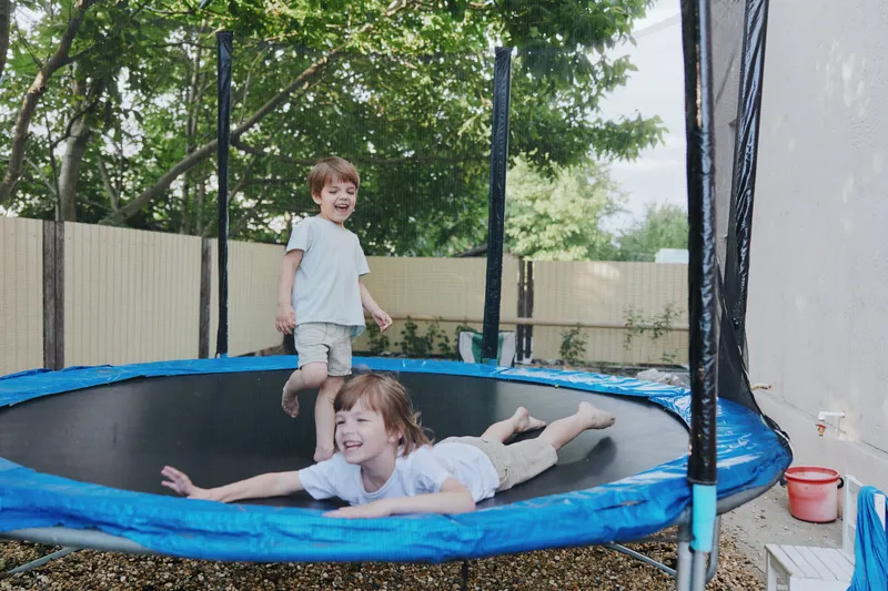 Happy children playing on a trampoline, enjoying outdoor fun and laughter in a sunny backyard setting filled with greenery and joy.