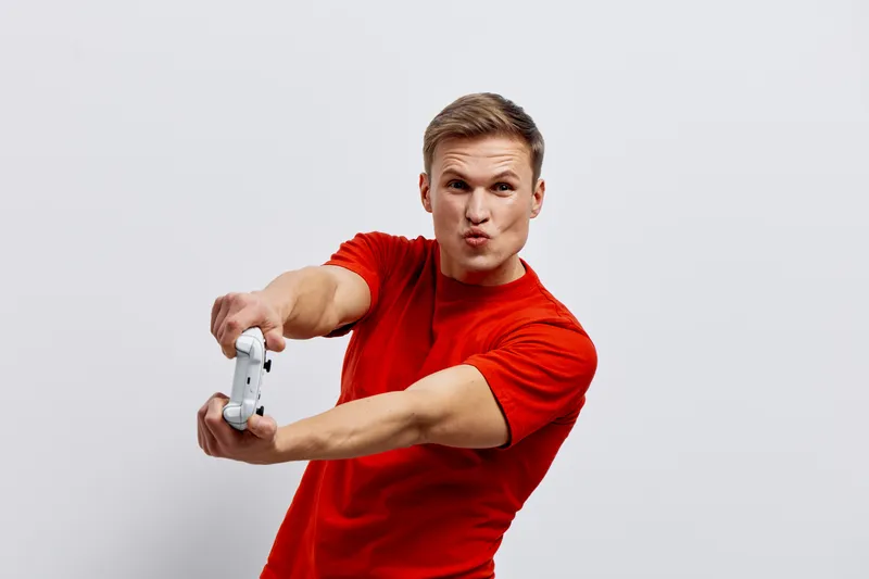 Young man in red t-shirt taking a selfie with smartphone, making a playful face, on plain light grey background, studio portrait, people lifestyle concept, male, casual, fun, modern style