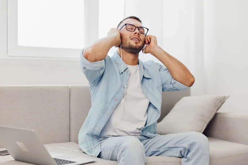 Relaxed man enjoying a moment of digital detox with headphones, focusing on mental well-being and soft masculinity in a cozy, modern setting.