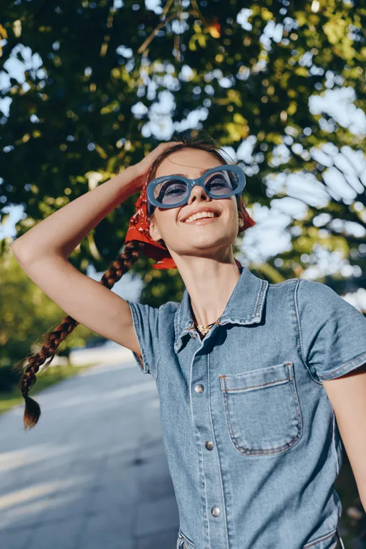 lifestyle woman wearing modern boho-western denim shirt with oversized sunglasses enjoys sunny day outdoors in vibrant film color tone and street style vibes