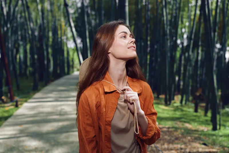 Woman portrait in a bamboo park on a sunlit path, nature scene showing relaxation and walking moment as a female traveler enjoys greenery and peaceful outdoor breeze.
