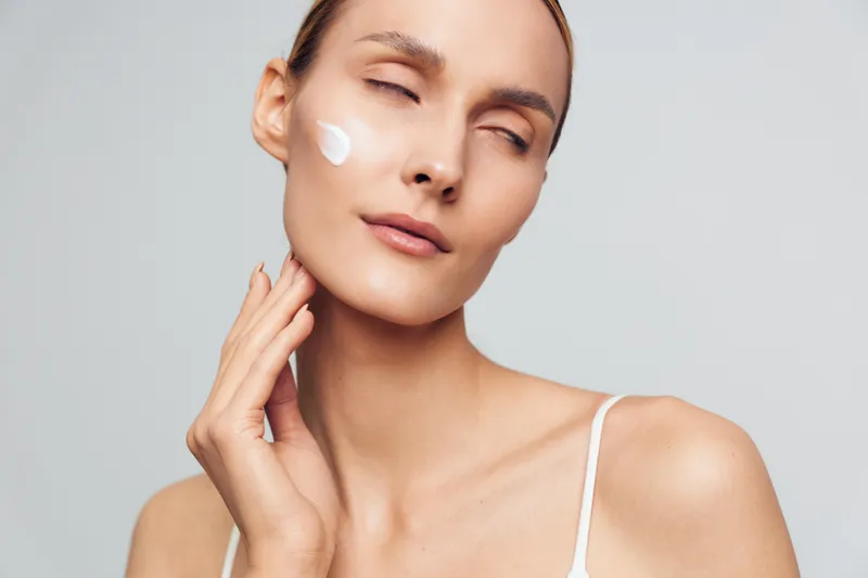 Woman skincare beauty portrait with cotton pad and moisturizer, self care for healthy skin in a spa style close up, calm female face, grey studio background soft light care