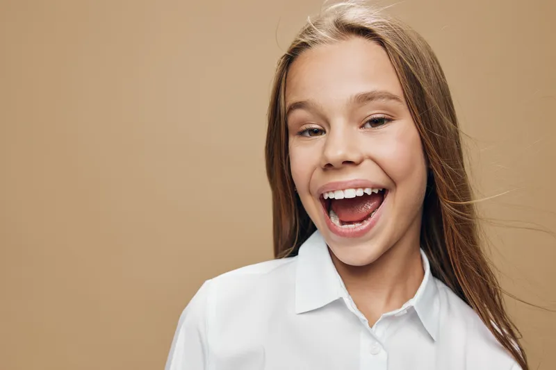 Smile girl portrait with long hair and white shirt on beige background. Happy female teenager with open mouth and joyful expression in studio lighting for positive mood.