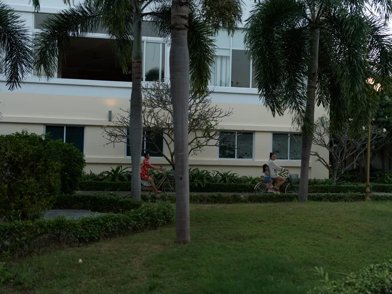 Relaxed woman walking with a child in a tropical garden near a modern building during evening light.