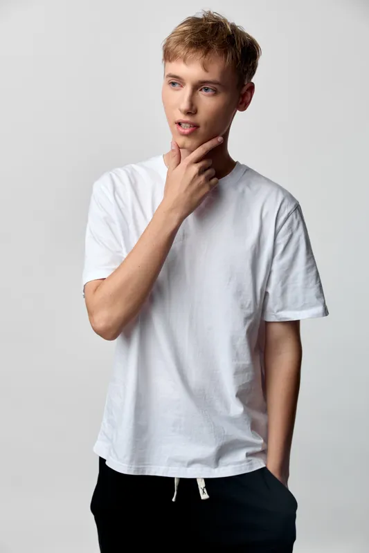 Thoughtful man in a white t shirt poses with hand on chin against a neutral backdrop, capturing a calm, casual, modern vibe perfect for lifestyle and fashion projects
