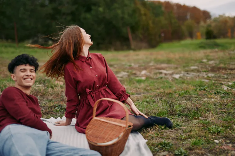 Young couple enjoying a candid picnic on a grassy meadow with a wicker basket and blanket, captured in an authentic moment conveying natural connection and credibility.