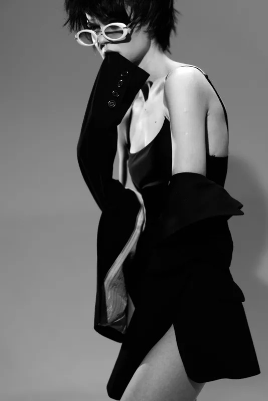 Black and white portrait of a stylish woman wearing glasses and elegant clothing with mysterious expression.
