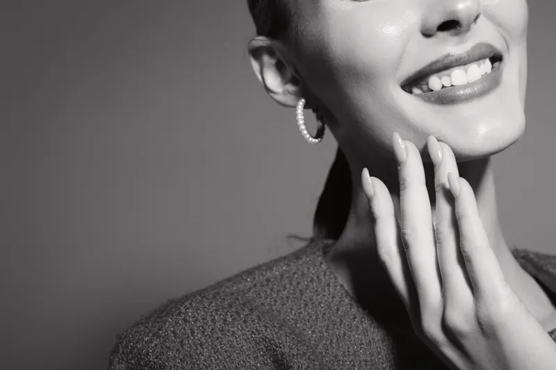 Close-up of smiling white woman with fair skin touching her face gently, showcasing natural beauty and happiness in black and white photography.