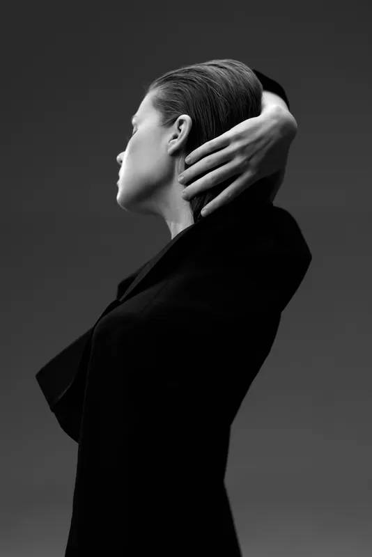Black and white portrait of a woman with slicked-back hair posing gracefully against dark background in stylish clothing