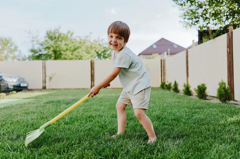 Playful boy enjoying outdoor fun while gardening, smiling brightly, in a sunny backyard filled with green grass and a vibrant atmosphere ideal for family activities.