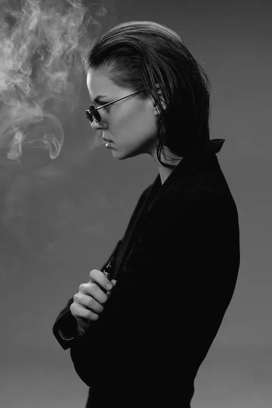 Black and white profile of a young woman wearing sunglasses with smoke creating a moody atmosphere.