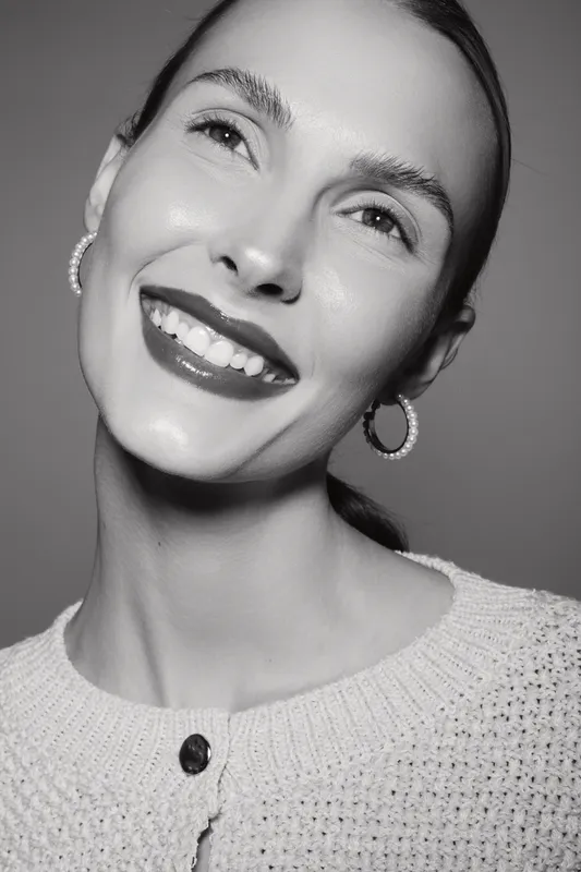 Happy caucasian woman with fair skin smiles broadly, wearing hoop earrings and knit sweater. Portrait in black and white studio, concept for joy and beauty.