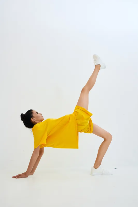 Active woman in yellow outfit performing dynamic floor exercise with one leg raised against white background, showcasing strength, balance, and flexibility.