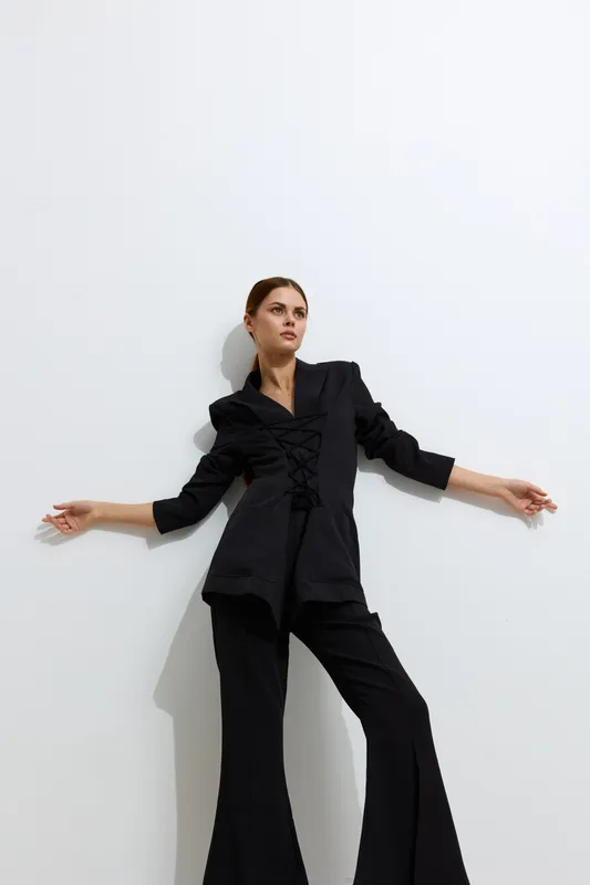 fashion woman dressed in black stylish suit posing confidently against a white wall with minimalistic aesthetic and strong lighting contrast