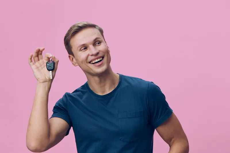 smiling young caucasian man hold car key look away wear blue t-shirt isolated pink background digital nomad concept