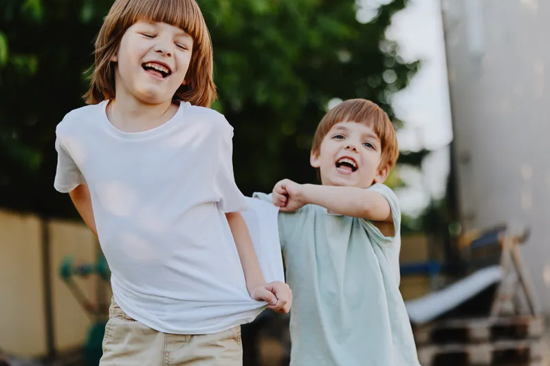 Two playful boys enjoying a sunny day outdoors, both laughing and running while wearing casual clothes. Their joy and energy are contagious, capturing childhood moments.