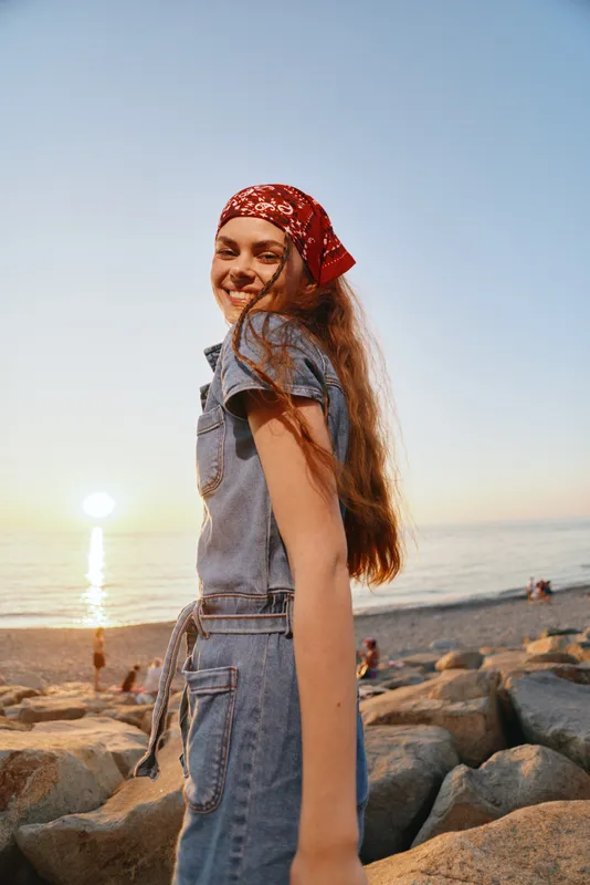 smiling woman in modern boho-western denim street style with red bandana at sunset beach, film color, lifestyle carefree joyful atmosphere outdoors